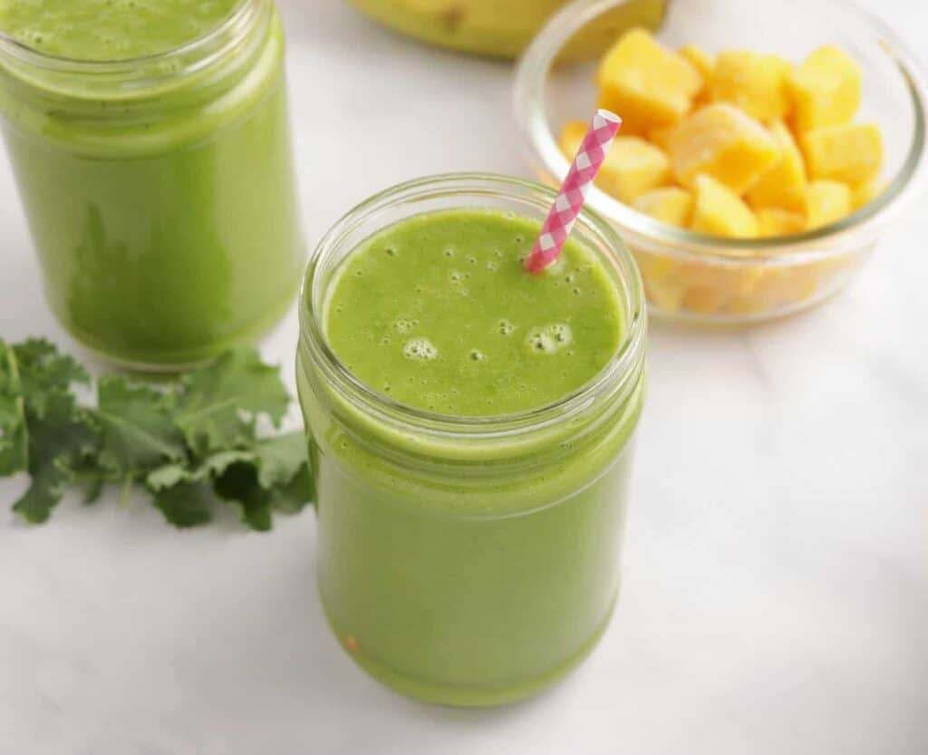 Dairy free mango smoothie in a glass jar with a pink straw.