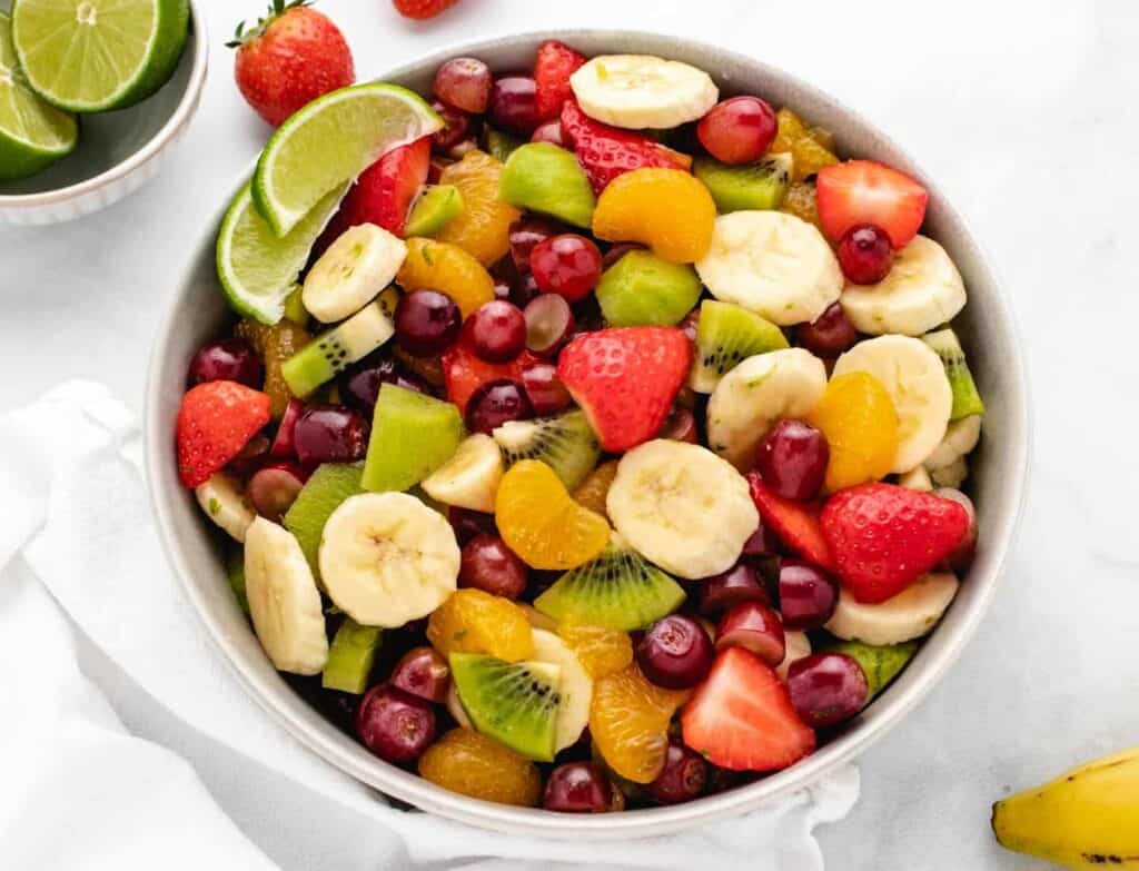 Vegan fruit salad with grapes, strawberries, sliced bananas, kiwis, and mandarin oranges in a bowl.