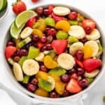 Vegan fruit salad with grapes, strawberries, sliced bananas, kiwis, and mandarin oranges in a bowl.