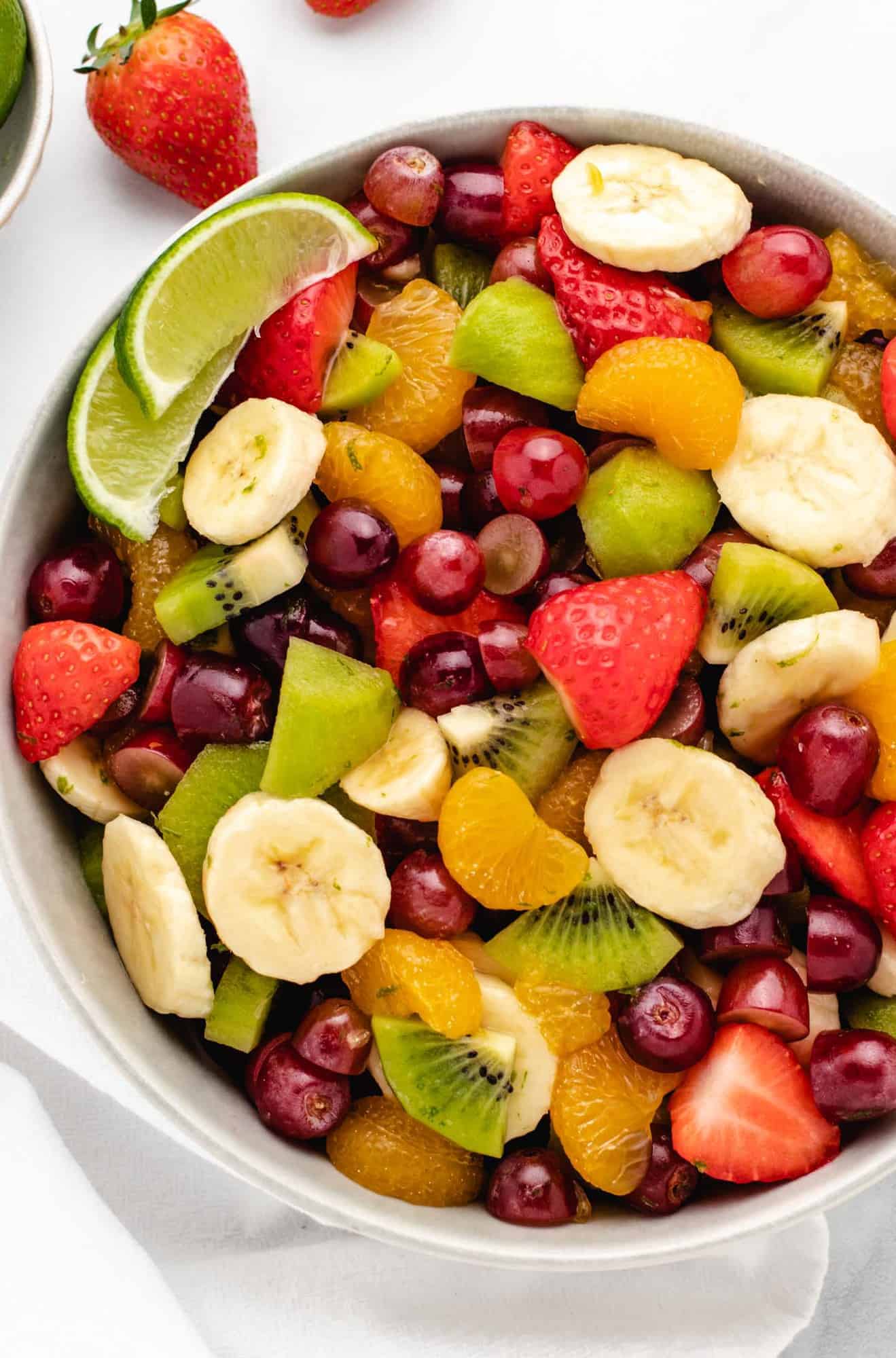 Vegan fruit salad with bananas, grapes, strawberries, kiwis, mandarin oranges in a bowl.