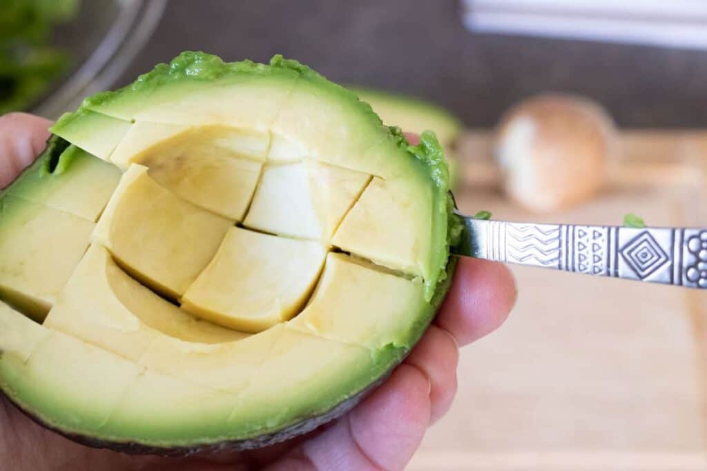 Scooping out the flesh of an avocado that has been cut in half and crosswise.