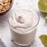 Smooth, creamy vegan cashew lime crema in a glass with sliced limes.
