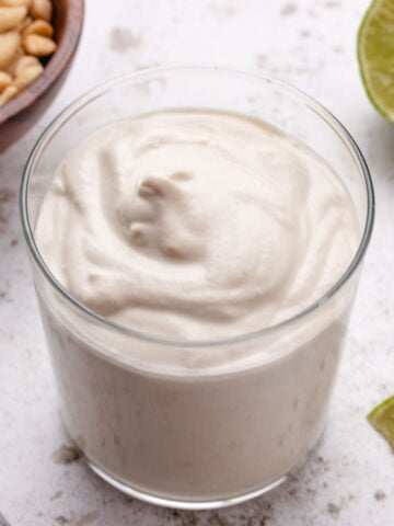 Smooth, creamy vegan cashew lime crema in a glass with sliced limes.