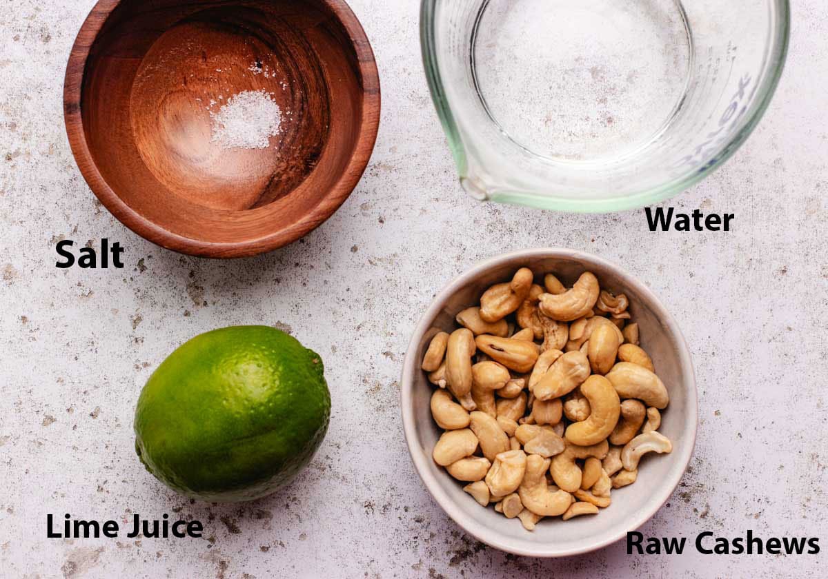 A bowl of salt, a glass of water, a lime, and a bowl of cashews.