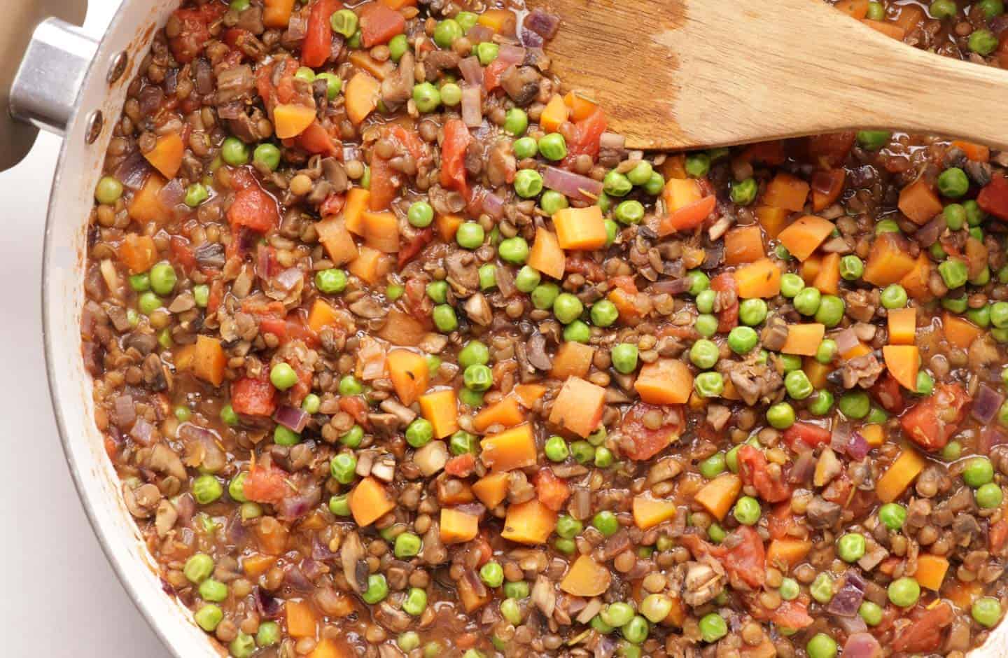 Cooked lentil filling with tomatoes and peas in a pan for a vegan shepherd's pie.