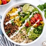 vegan taco bowl with lentil taco meat, brown rice, limes, corn, tomatoes in a bowl