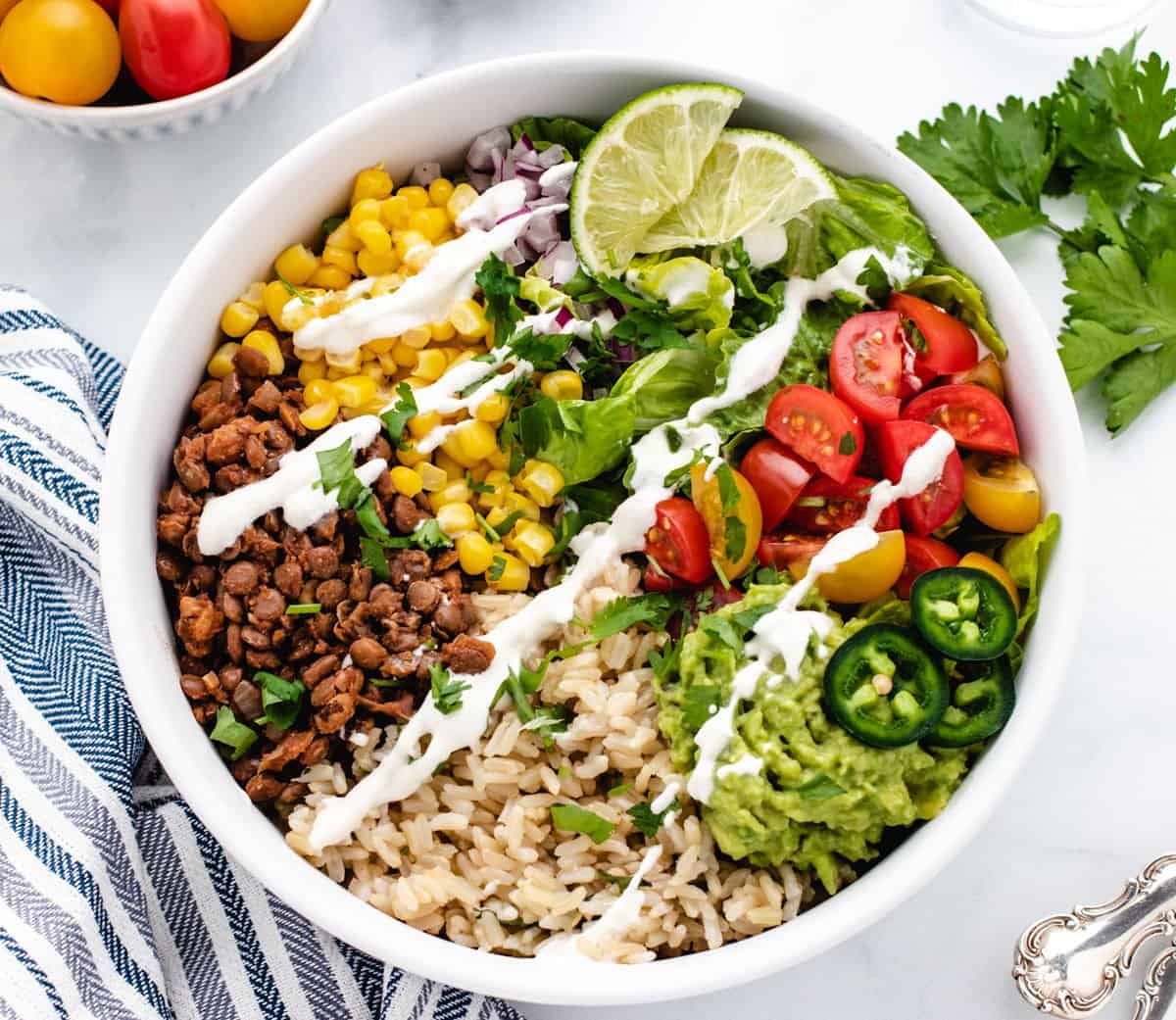 Taco bowl with corn, lentil taco meat, rice, guacamole, cherry tomatoes, and lime slices.