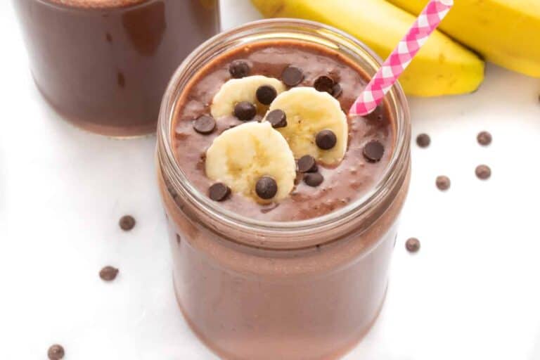 Dairy-free chocolate banana smoothie in a glass with a straw and banana slices.