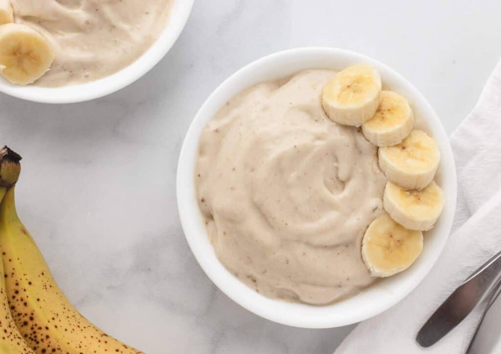 Banana ice cream in a white bowl with sliced bananas.