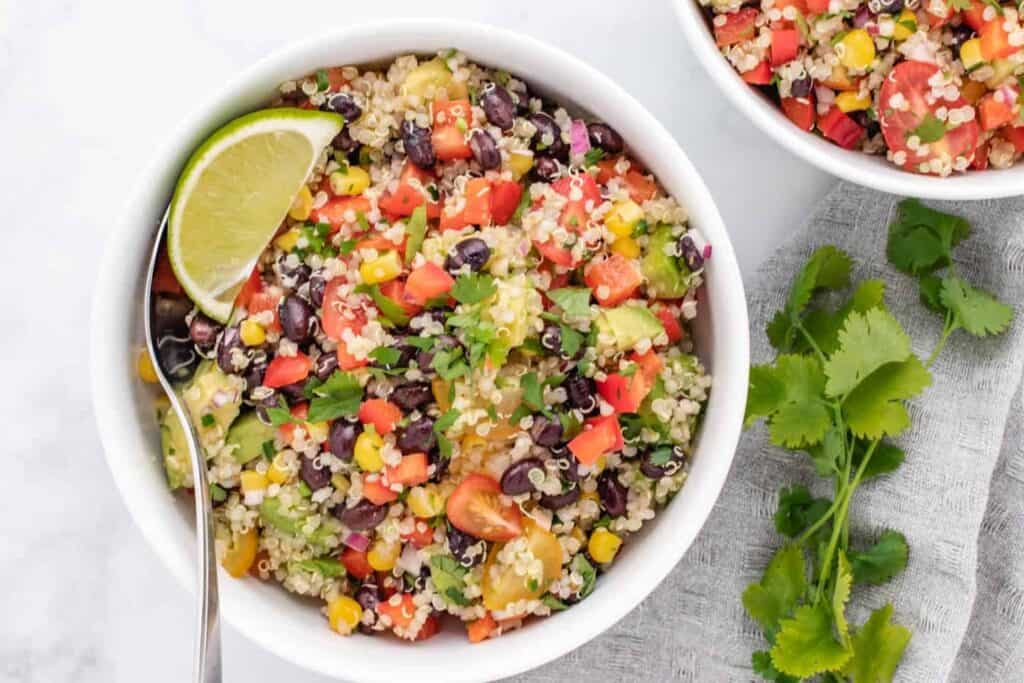 Zesty quinoa salad with black beans and a lime wedge in a white bowl.