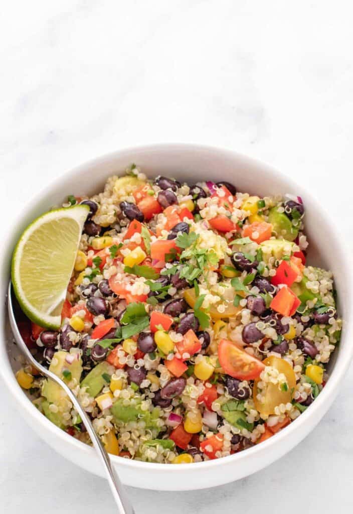 Zesty quinoa salad with black beans and lime wedges in a bowl.