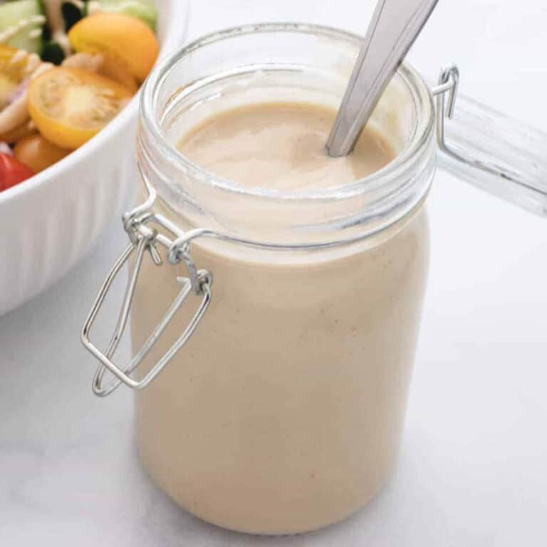 Tahini dijon mustard dressing in a glass jar with a spoon.