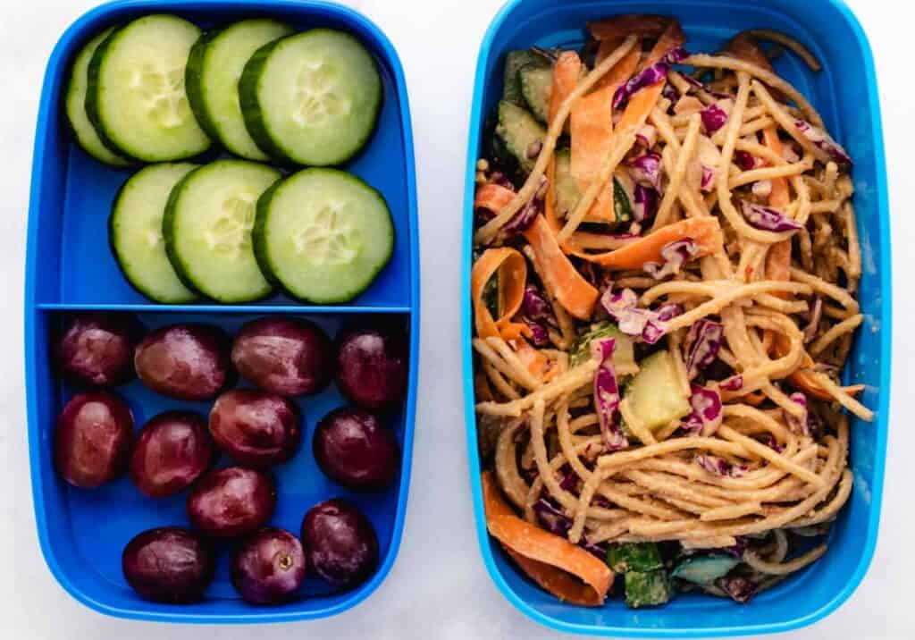 Peanut noodles with cucumber, carrots, and red cabbage in half the bento box and grapes and cucumbers in the half.