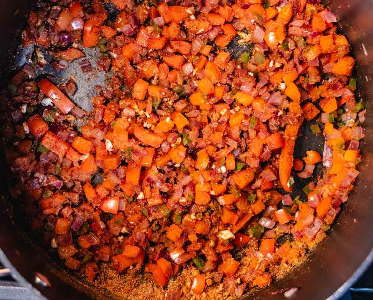 Cooked onions, bell peppers, and jalapeno with garlic and spices in a pot.