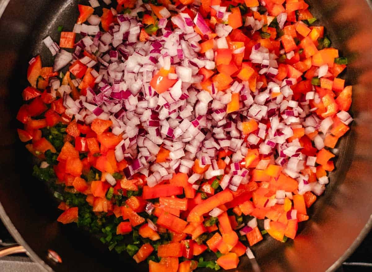 Diced red onions, red bell peppers, and jalapeno in a pot.