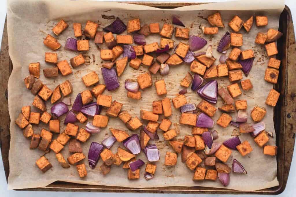 Roasted cubed sweet potatoes and red onions on a baking tray.