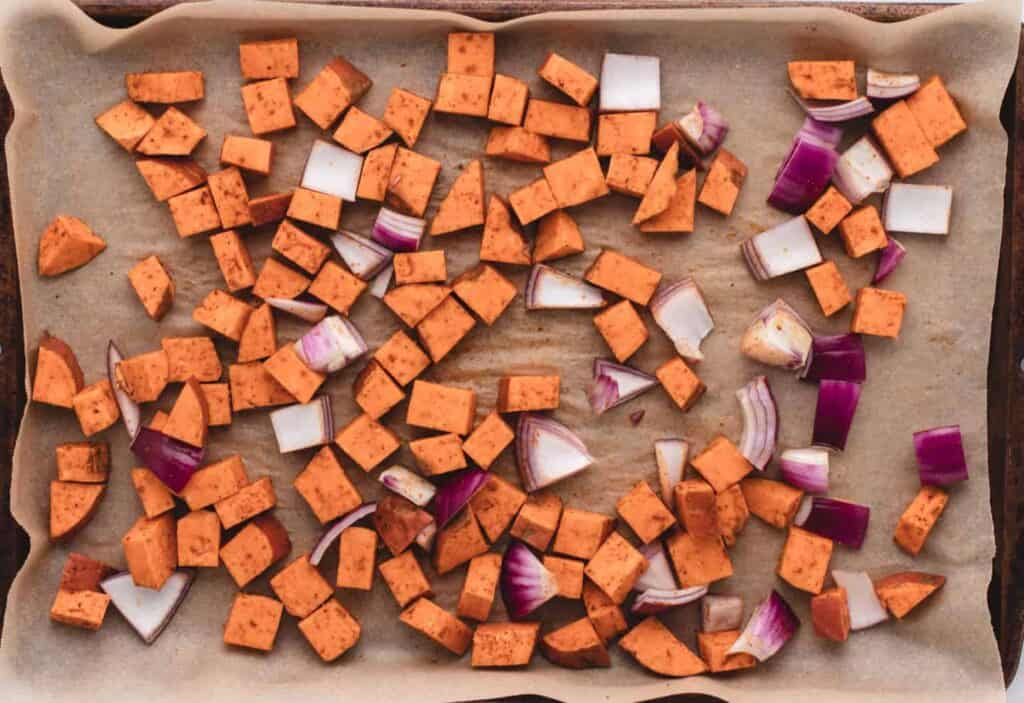 Cubed sweet potato and red onions ready for roasting on a baking tray.