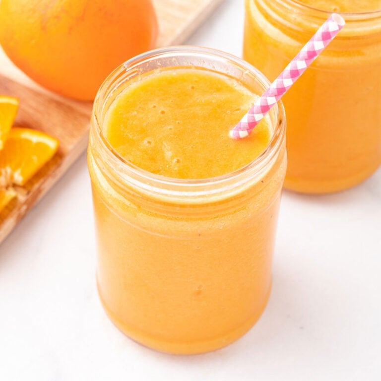 Orange carrot ginger smoothie in a glass with a straw.