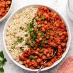 Tomato chickpea stew in a white bowl with brown rice and chopped cilantro.