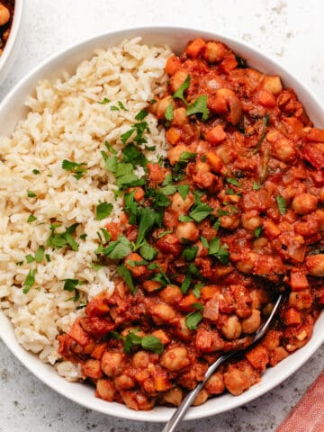 Tomato chickpea stew in a white bowl with brown rice and chopped cilantro.