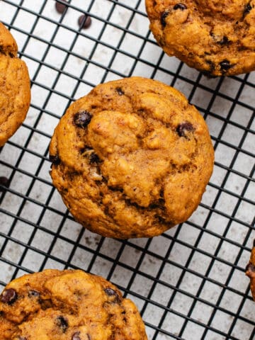 Vegan oil free pumpkin muffins on a cooling rack with chocolate chips.