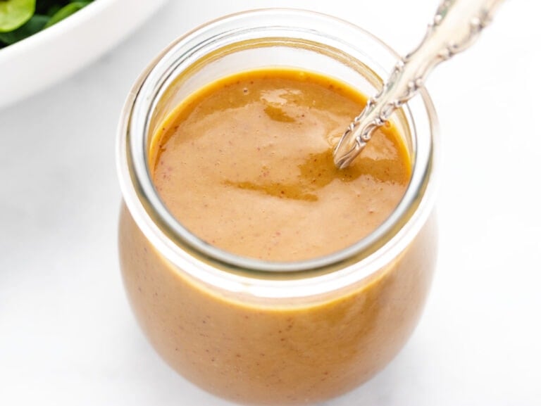 Spicy brown mustard dressing in a glass jar with a spoon.