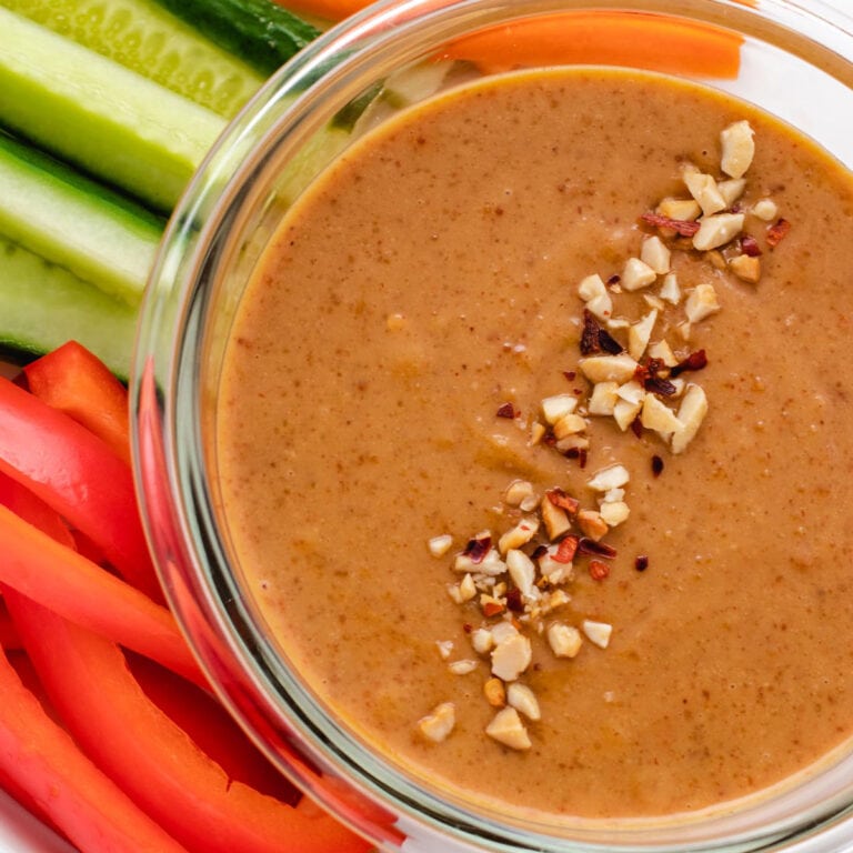 Peanut dressing in a glass bowl with crushed peanuts on top.