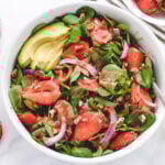 Vegan strawberry spinach salad in a bowl with avocado and sliced red onion.