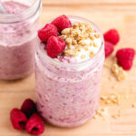 Raspberry overnight oats in glass jar with raspberries and granola on top.