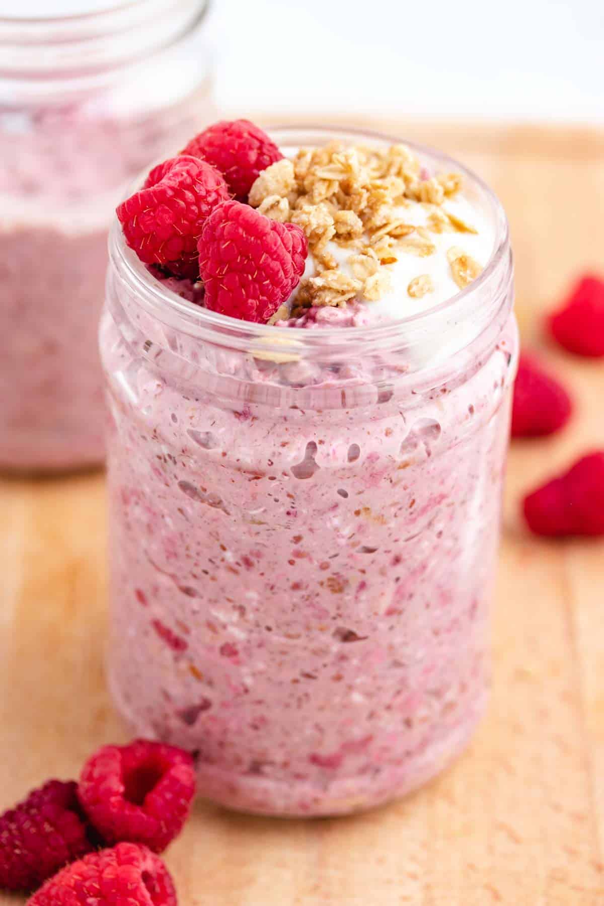 Overnight oats with raspberries in a jar with granola and raspberries on top.
