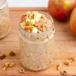Overnight applesauce oats in a glass jar with diced apples and chopped walnuts on top.