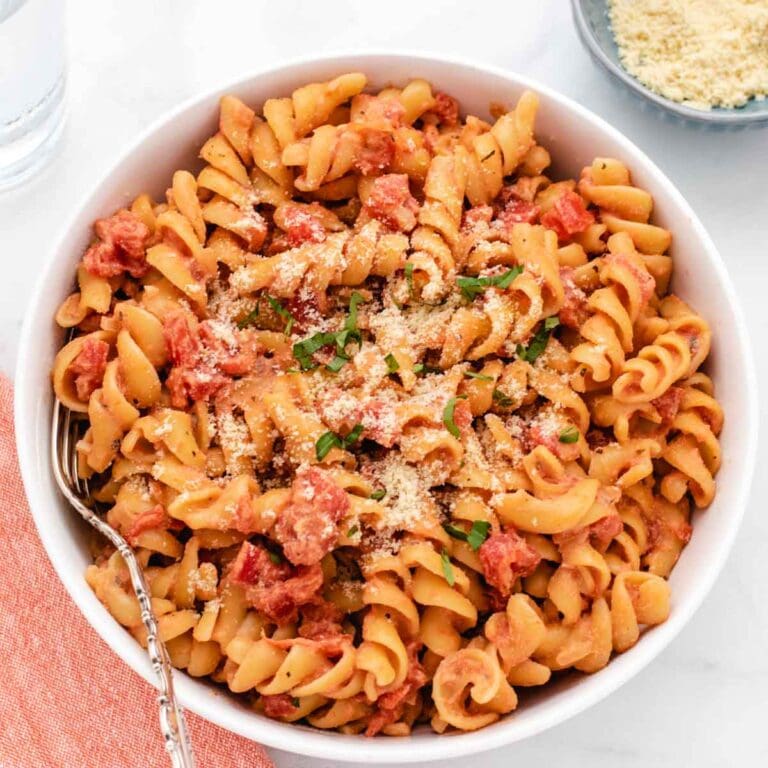 Vegan tomato pasta in a white bowl with a fork.
