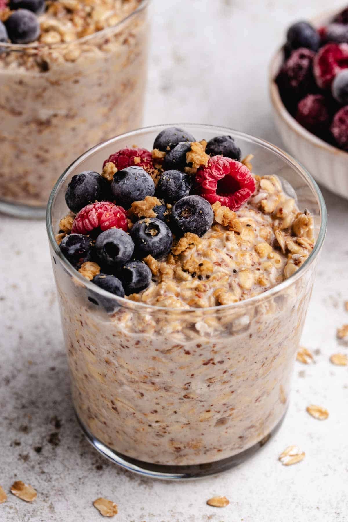 Overnight oats with frozen berries in a glass with frozen berries and granola on top.