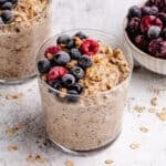 Overnight oats with frozen fruit in a glass with frozen berries and granola on top.
