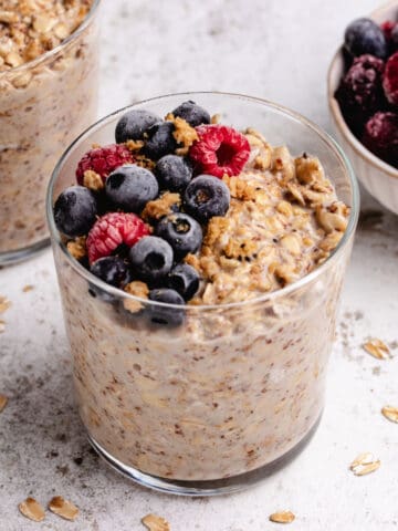 Overnight oats with frozen fruit in a glass with frozen berries and granola on top.