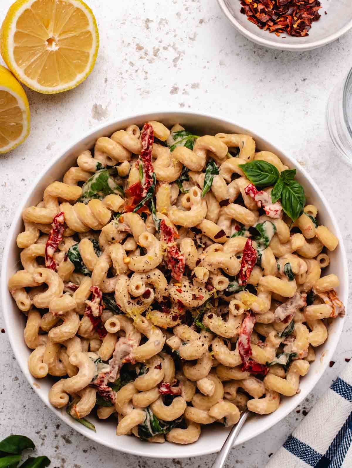 Creamy pasta tahini in a white bowl with sun-dried tomatoes and spinach.