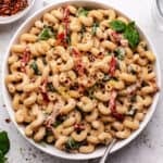 Tahini pasta in a white bowl with sun-dried tomatoes and spinach.