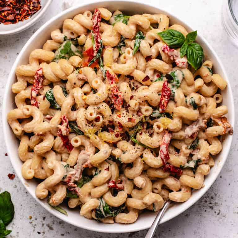 Tahini pasta with sundried tomatoes and spinach in a bowl with a fork.