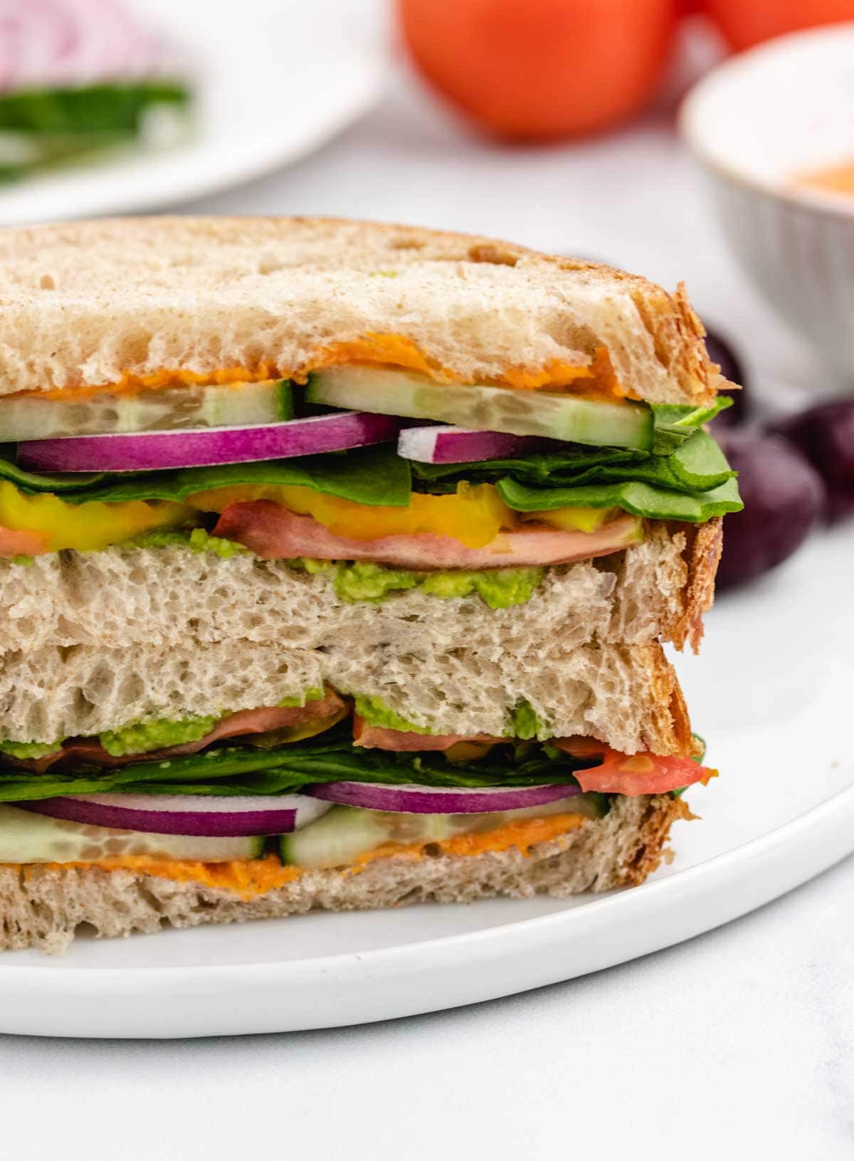 Hummus cucumber sandwich with red onion and tomato on a plate.