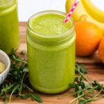 Arugula smoothie in a jar with a straw and oranges in the background.