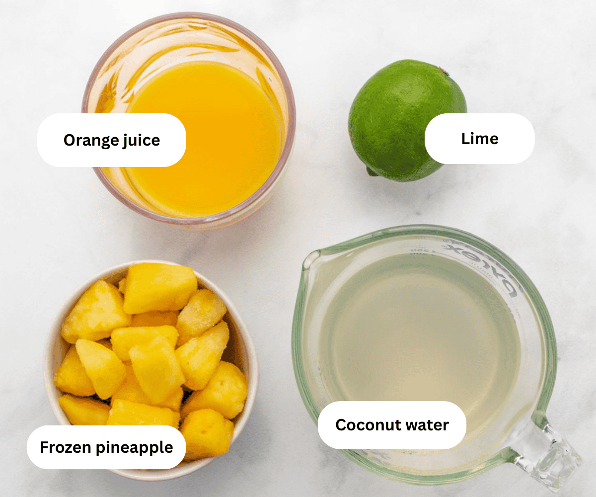 Orange juice, lime, frozen pineapple, and coconut water on a table.
