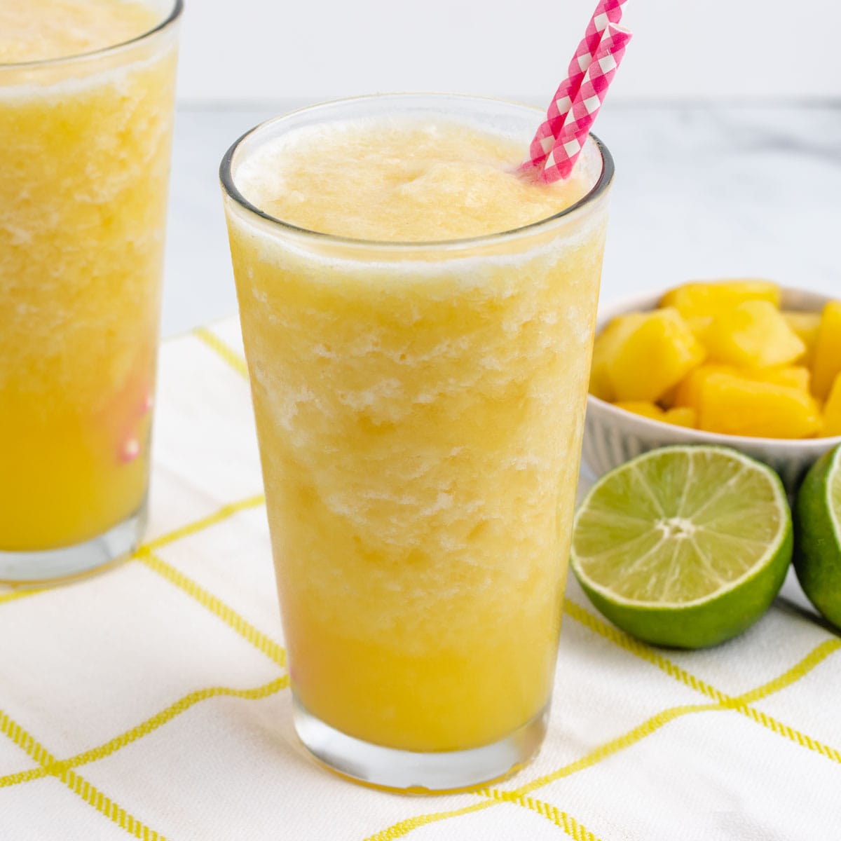 Pineapple slushie with pink straws in a glass with limes in the background.