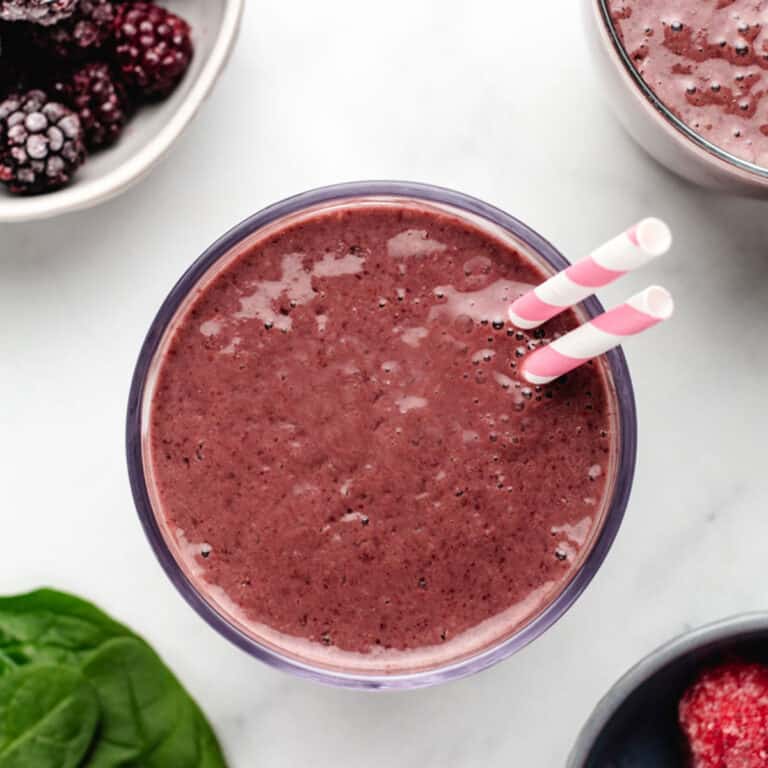 Blackberry strawberry smoothie in a glass with two straws.