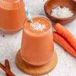 Carrot banana smoothie in a glass with shredded coconut on top.