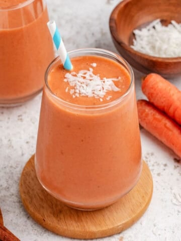 Carrot banana smoothie in a glass with shredded coconut on top.