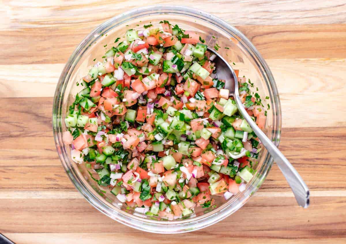 Cucumber pico mixed together in a glass bowl with a spoon.