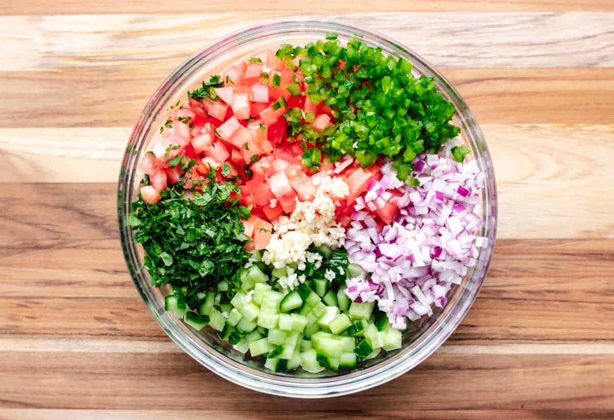 Diced cucumber, tomatoes, red onion, jalapeno, garlic, and cilantro in a bowl.