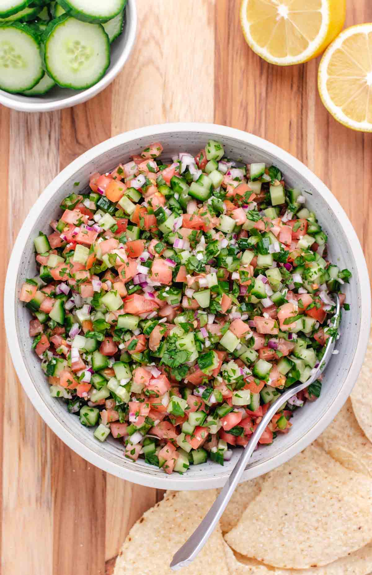 Cucumber pico de gallo in a bowl with a spoon and chips to the side.