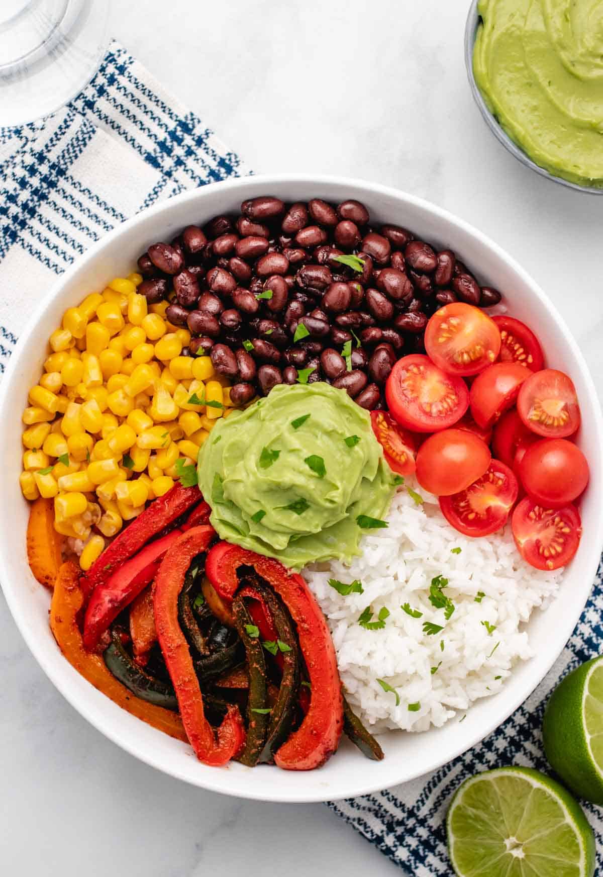 Veggie fajita bowl with rice, black beans, veggies, corn, cherry tomatoes, and avocado lime crema.