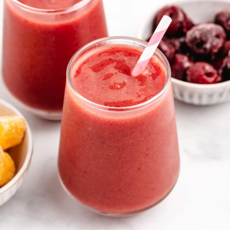 Cherry mango smoothie in a glass with a straw.
